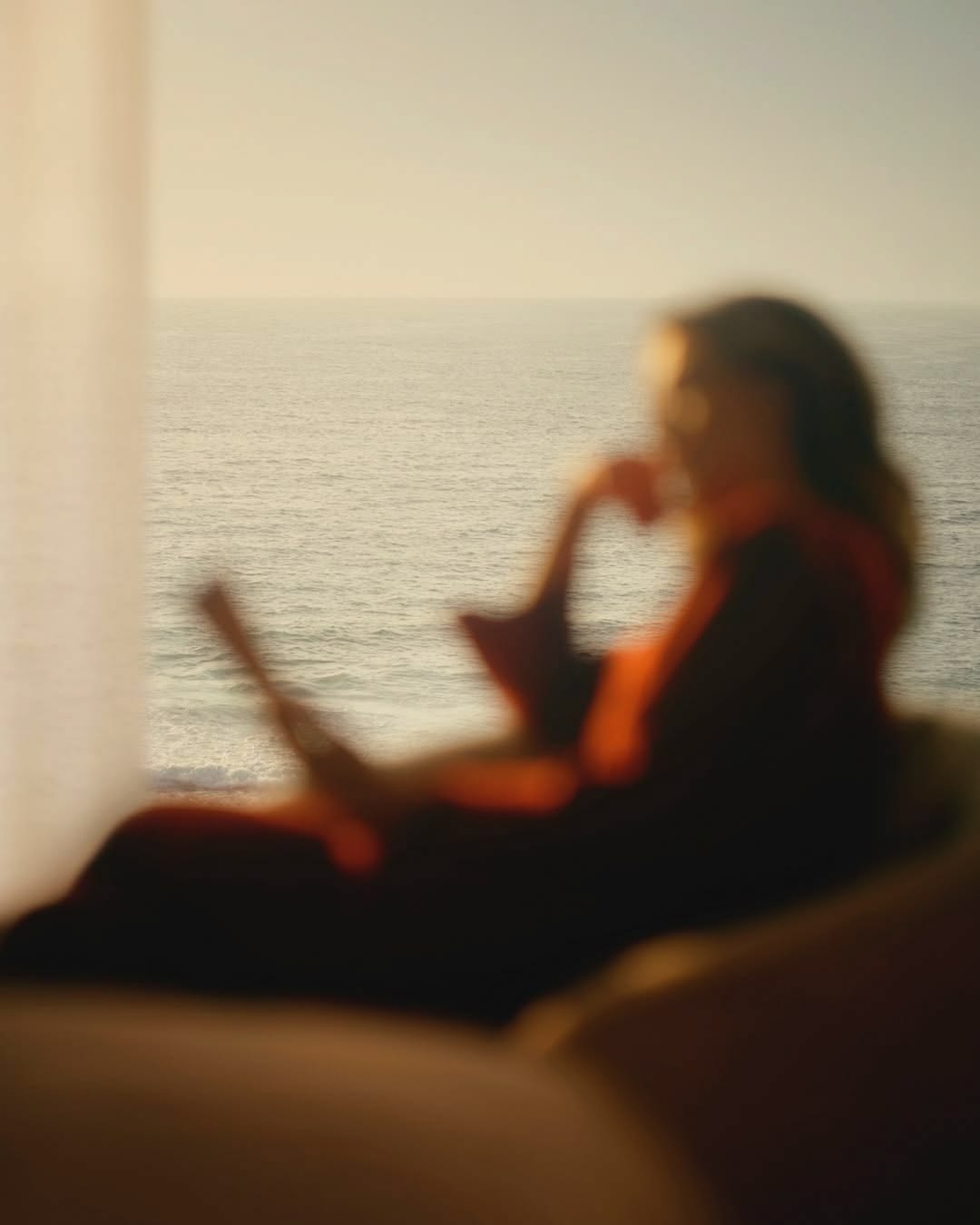 A woman with coffee by a window overlooking the sea